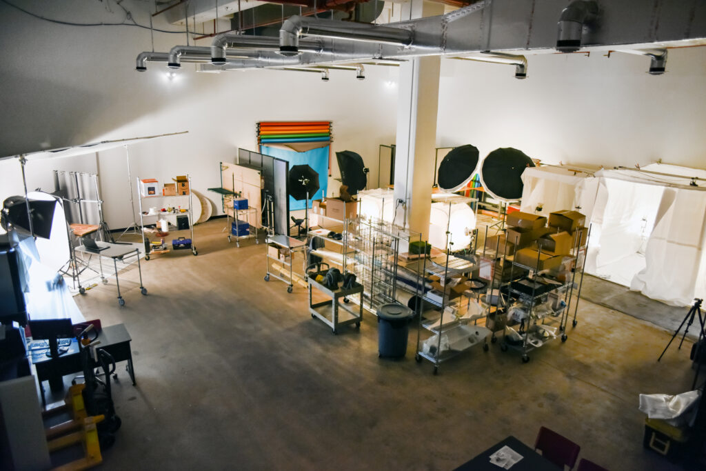 Low lit aerial view of product photography studio displaying lights, tripods, wire racks full of product, computers and cameras.