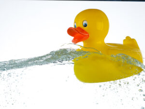 Product photography image of a rubber duck dropping into water with a big splash.