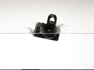 Product photography image of a camera dropping into water with a big splash.