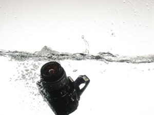 Product photography image of a camera dropping into water with a big splash.