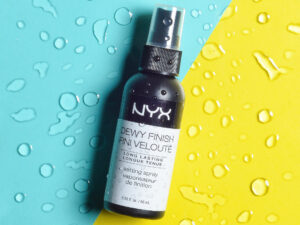 Hero image of an NYX spray bottle, shot on a colorful background with water droplets